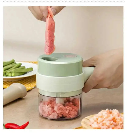 Hand using electric mini food chopper to mince raw meat on kitchen table with vegetables