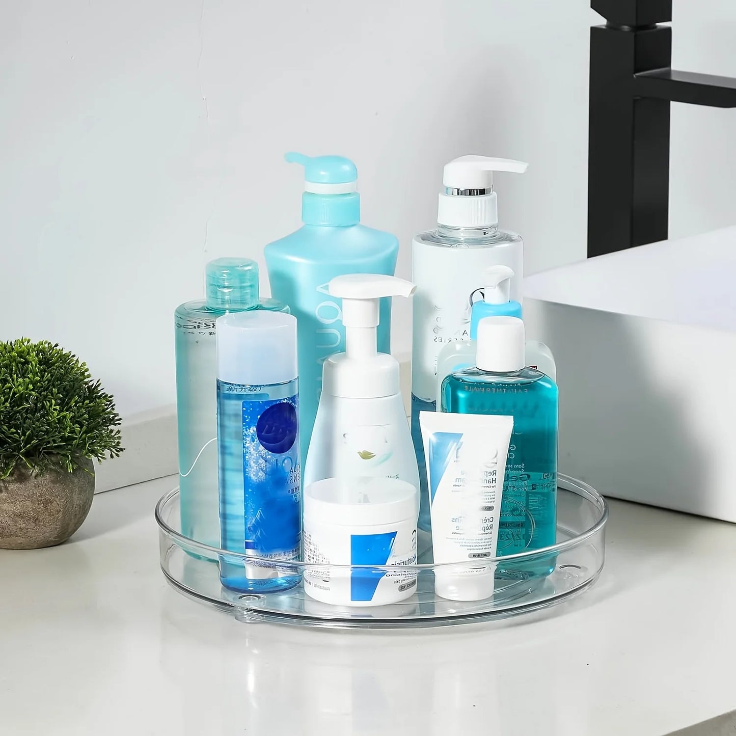 Clear rotating organizer tray with various blue and white skincare and cleaning bottles on bathroom counter