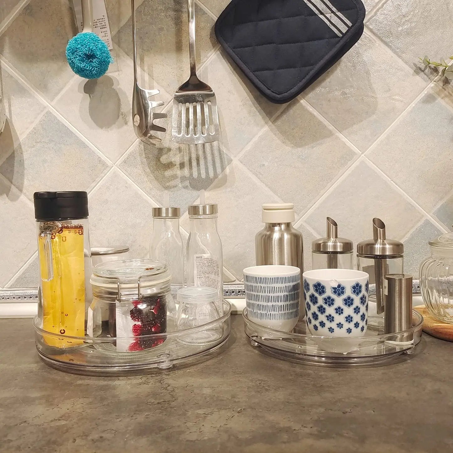 Kitchen countertop with clear lazy susan organizers holding cups, bottles, jars, and stainless steel containers