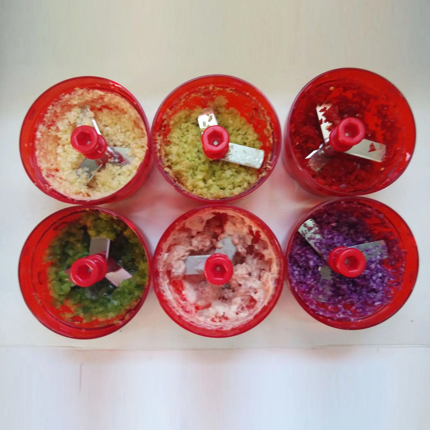 Six red food choppers with finely chopped ingredients in various colors on white surface