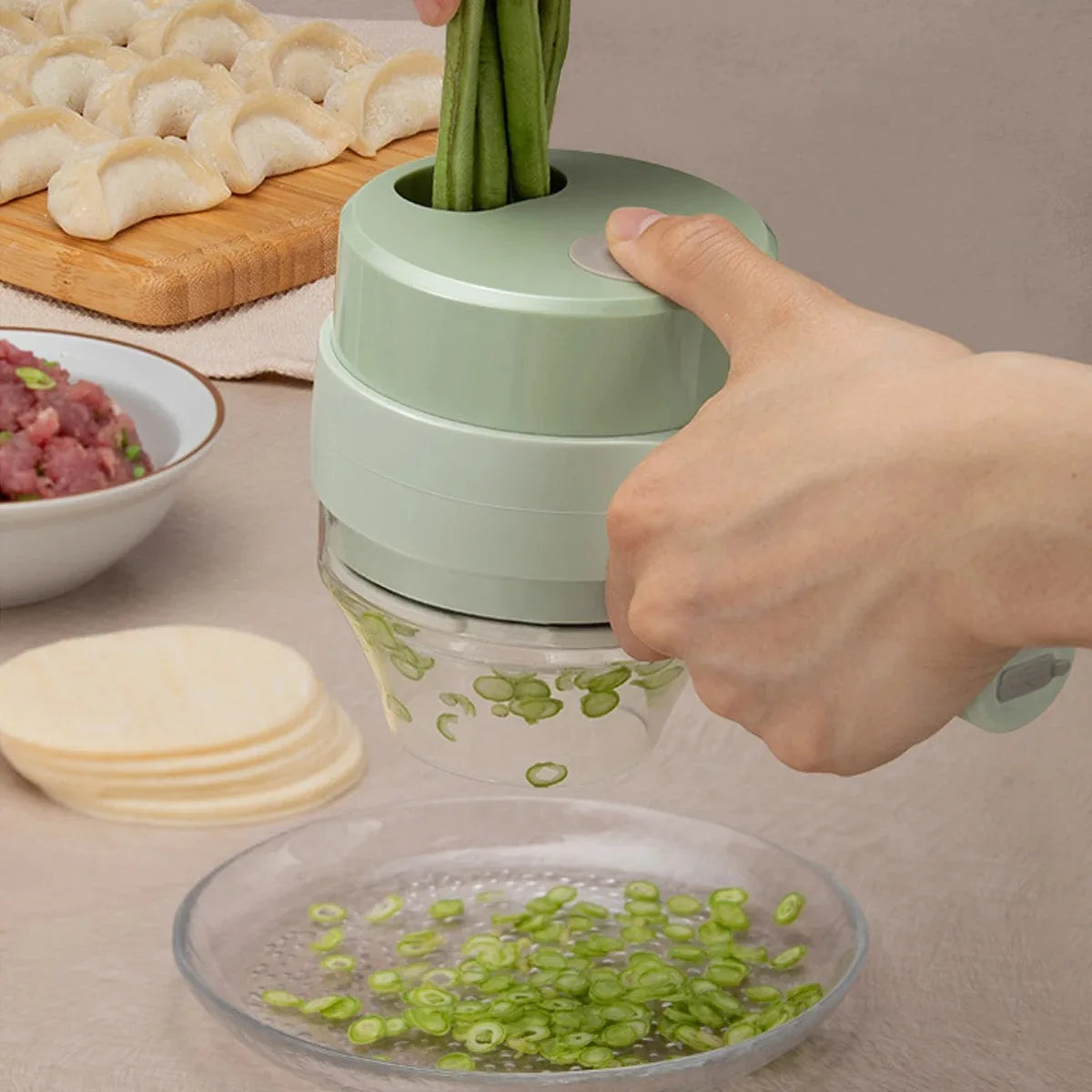 Hand using green manual vegetable slicer to cut green onions with dumplings, minced meat, and wrappers nearby